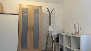 A room with a wooden wardrobe, a standing fan, and a cactus on a shelf.