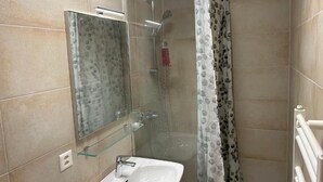 A bathroom with a glass shower enclosure, a white sink, and a mirror.