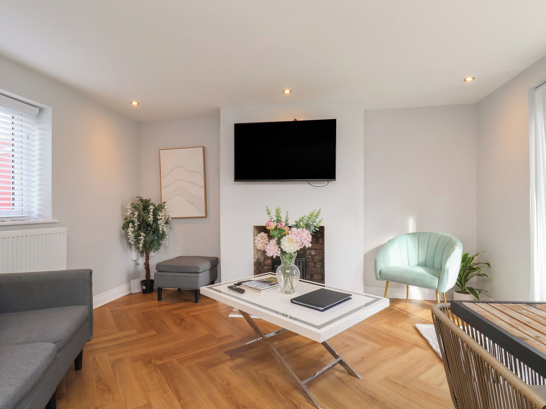 Una sala de estar moderna con un televisor de pantalla plana, un sofá gris, una mesa de centro con un jarrón de flores y un sillón azul claro.