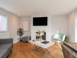 Una sala de estar moderna con un televisor de pantalla plana, un sofá gris, una mesa de centro con un jarrón de flores y un sillón azul claro.