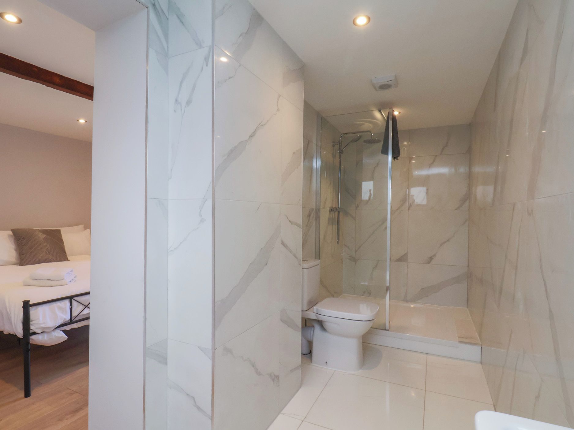 A modern bathroom with a glass-enclosed shower, a toilet, and a bed with white linens.