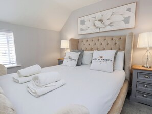 Un lit bien fait, avec du linge de lit blanc et des oreillers, une tête de lit capitonnée et, au-dessus, un tableau floral encadré.