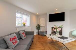 Una sala de estar moderna con un sofá gris, una mesita con un florero, un sillón gris y un televisor montado en la pared.