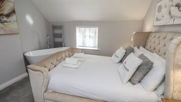 A bedroom with a large bed, a bathtub, and a window with blinds.