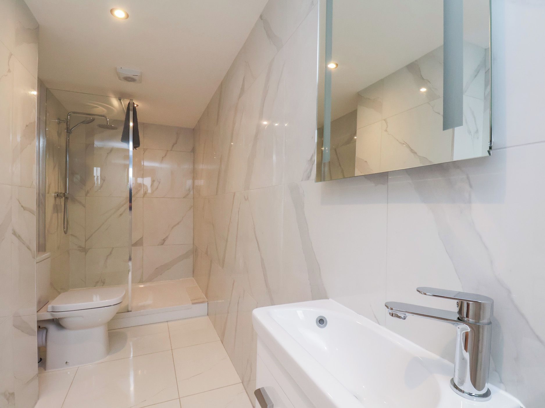 Un bagno moderno con cabina doccia in vetro, un water bianco e un lavandino bianco con rubinetto cromato.