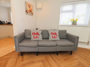 Ein graues Sofa mit zwei Kissen, die roten Text zeigen, eine weiße Wand, ein Fenster mit Jalousien und eine Heizung.