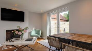 Una sala moderna con comedor, televisor de pantalla plana en la pared, chimenea y vistas al exterior.