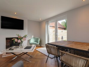 Una sala moderna con comedor, televisor de pantalla plana en la pared, chimenea y vistas al exterior.
