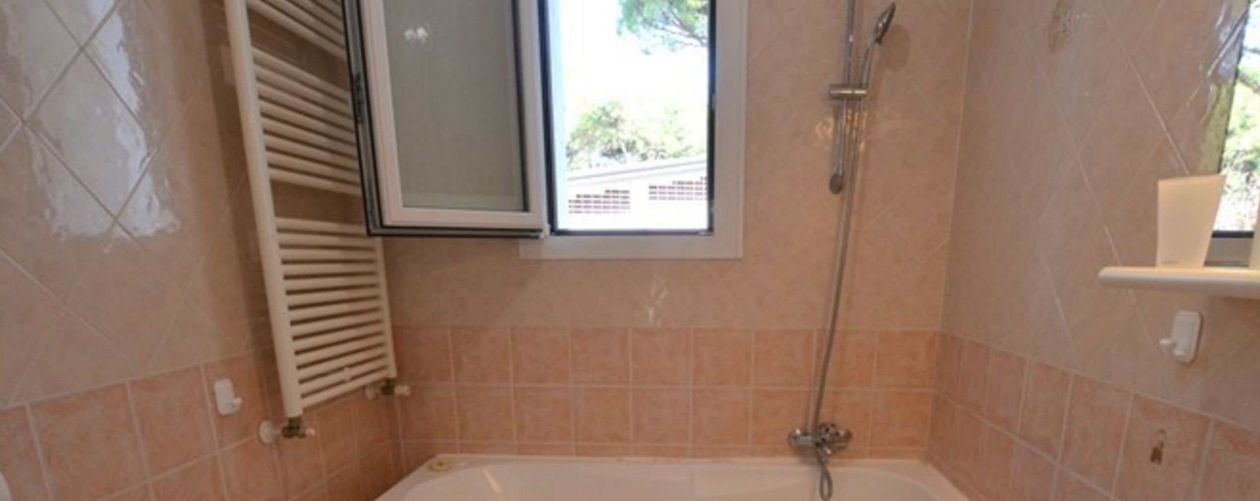 A bathroom with a bathtub, a window, and a shower.