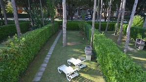 Un jardín con un sendero pavimentado, setos podados y tres sillas blancas para lounge.