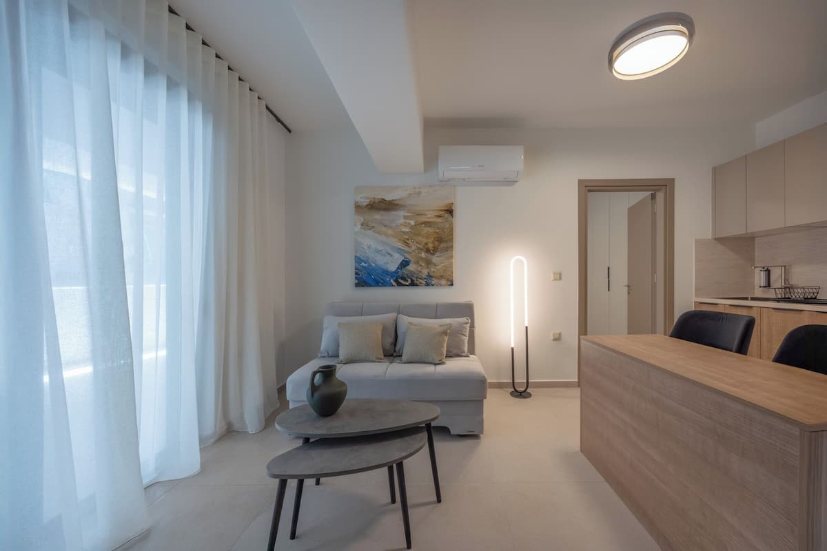 A modern living room with a sofa, a small table, and a kitchen area with cabinets and a countertop.
