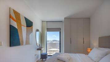A modern hotel room with a bed, a large abstract painting, a wardrobe, a balcony with a view, and a small round table.