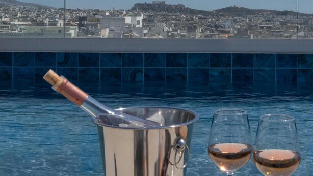 A poolside setting with a metal bucket containing a bottle, two glasses of wine, and a cityscape view in the background. - Sokio Attiki Hotel, Bw Premier Collection (Athens)