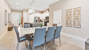 A modern kitchen with white cabinets, stainless steel appliances, and a dining area with a white table and blue chairs. - Contemporary Summerville resort home - 5 miles to Disney (Kissimmee)