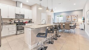 A modern kitchen with white cabinets, stainless steel appliances, and a central island with bar stools. - Contemporary Summerville resort home - 5 miles to Disney (Kissimmee)