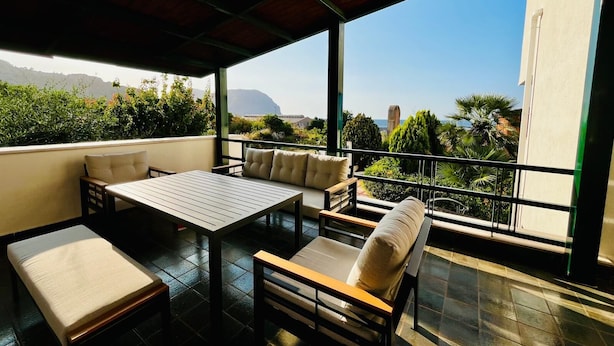 A covered outdoor seating area with a table and chairs, overlooking a scenic view of mountains and a body of water. - VILLA TIMOLEONTE - ADDAURA (Palermo)