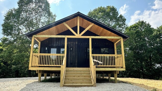 Une cabane en bois dotée d’un porche et d’un escalier menant à l’entrée.