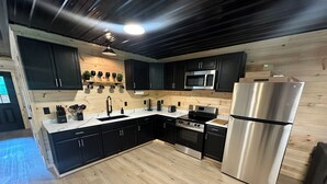 Une cuisine moderne avec des meubles de couleur sombre, des appareils en acier inoxydable, un plancher en bois et un luminaire au plafond.