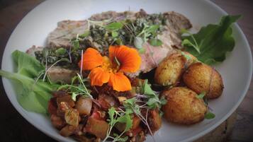 A plate with roasted meat, potatoes, and a flower garnish.