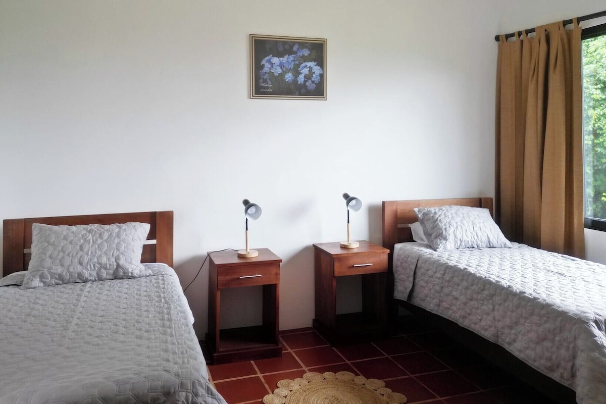 Een kamer met twee bedden, elk met een nachtkastje en een lamp. Daarboven hangt een ingelijst schilderij aan de muur.