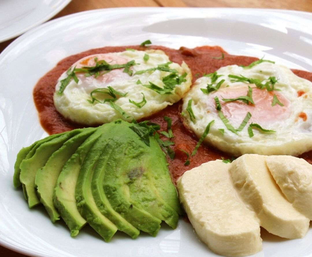 Un plato con aguacate en rodajas, dos huevos pochados y salsa roja.