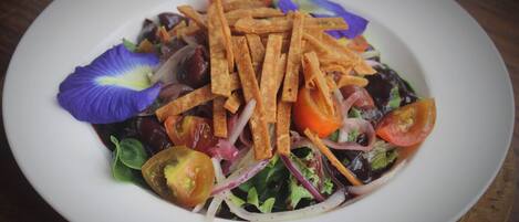 A white plate with a salad, including lettuce, tomatoes, and croutons, on a wooden table.