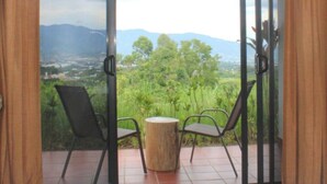 A balcony with two chairs and a small round table, overlooking a lush green landscape with distant mountains.
