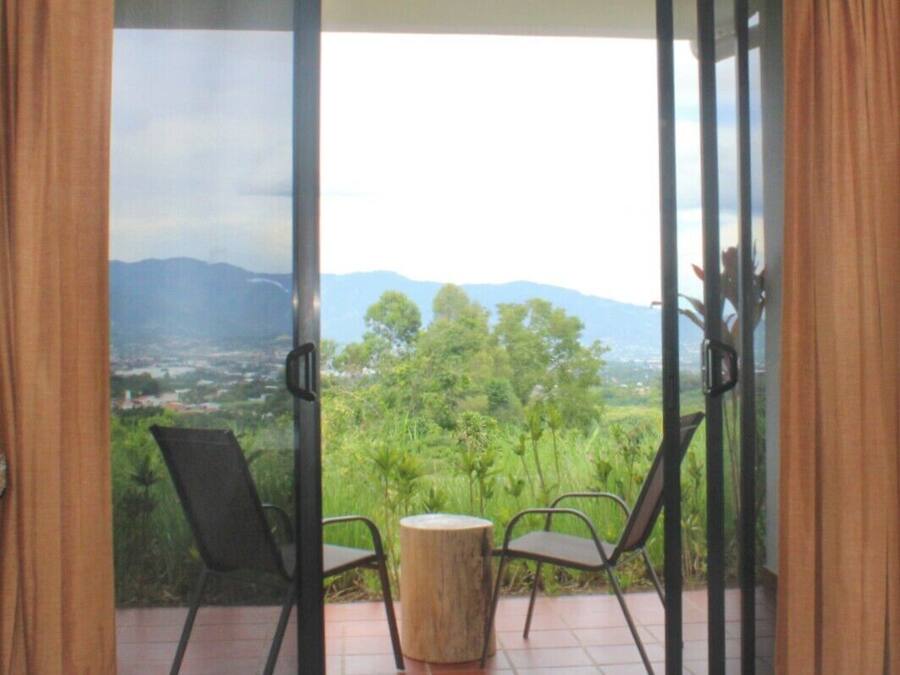 Varanda com duas cadeiras e uma mesa redonda pequena, com vista para uma paisagem verdejante e montanhas ao longe.