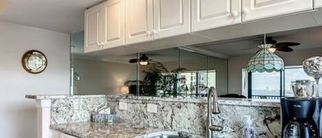 A kitchen with white cabinets, granite countertops, stainless steel sinks, and a coffee maker.