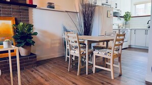 A modern kitchen with white cabinets, a wooden dining table with patterned chairs, and a brick accent wall.