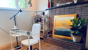 A modern office space with a white desk, chair, and lamp. A bookshelf and a fireplace with a painting are also visible.