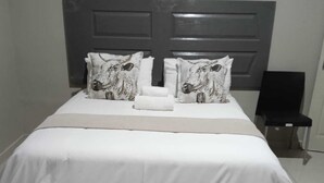 Una cama bien hecha con ropa de cama blanca y dos almohadas decorativas con estampados de animales.