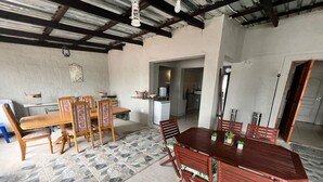 Un comedor con una gran mesa de madera y sillas, una cocina al fondo y piso de baldosas.