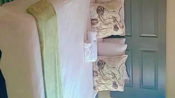 Un llit ben arropat amb coixins i una manta, una taula rodona petita, i una porta grisa en una habitació amb parets beix.