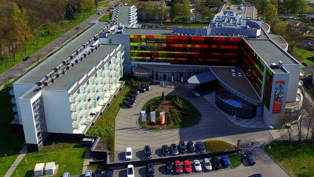 A modern hotel with a distinctive colorful facade, a central courtyard, and a parking lot with several cars.