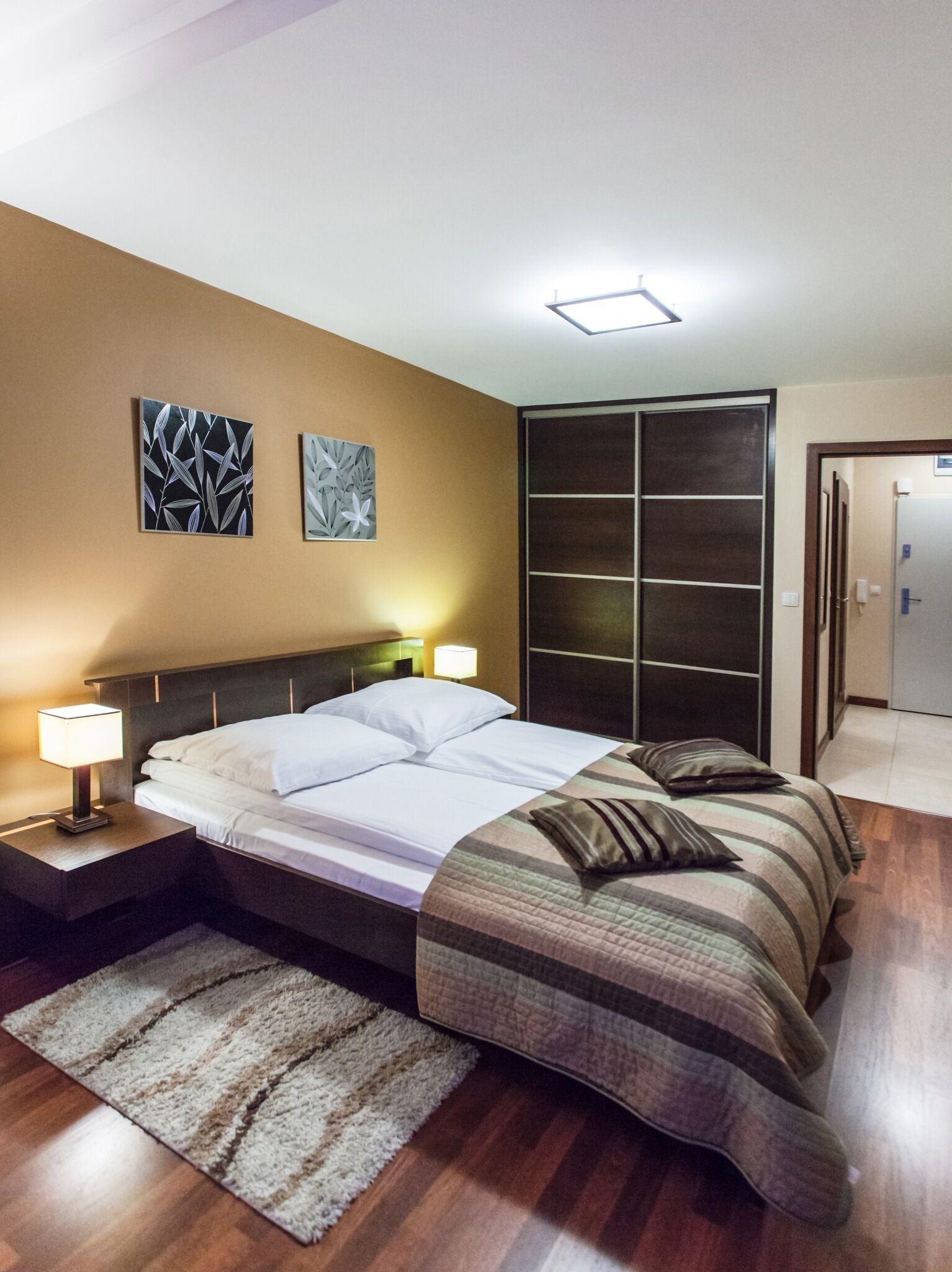 Un dormitorio moderno con una cama grande, dos lámparas de noche, un cabecero oscuro y vistas a un armario.