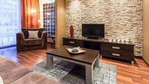 A modern living room with a stone wall, a flat-screen TV, a brown sofa, and a coffee table.