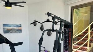 Een sportschool thuis met een loopband, een gewichtbank en een multifunctionele fitnessapparaat.
