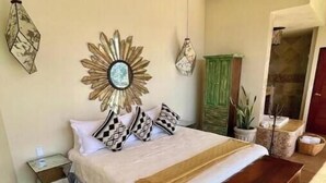 Een slaapkamer met een bed, een houten bankje, een plafondventilator, decoratieve muurkunst en een groene kast.