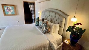 A neatly made bed with a tufted headboard, a bedside table with a lamp, and a potted plant. - Scenic views in Downtown/Romantic Zone (Puerto Vallarta)