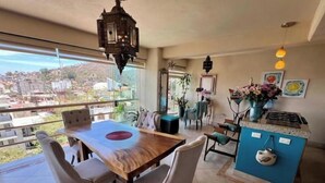 A dining area with a wooden table and chairs, a hanging lantern, and a view of the city through large windows. - Scenic views in Downtown/Romantic Zone (Puerto Vallarta)
