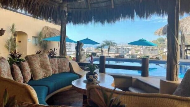 A lounge area with a thatched roof, a pool, and a view of a resort complex. - Scenic views in Downtown/Romantic Zone (Puerto Vallarta)