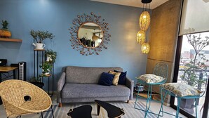 A modern living room with a grey sofa, two black coffee tables, a wicker chair, and a blue chair with a plant.