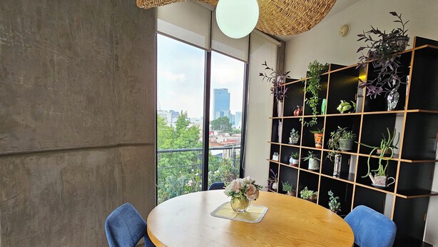 A modern dining area with a round wooden table, blue upholstered chairs, and a woven ceiling light fixture.