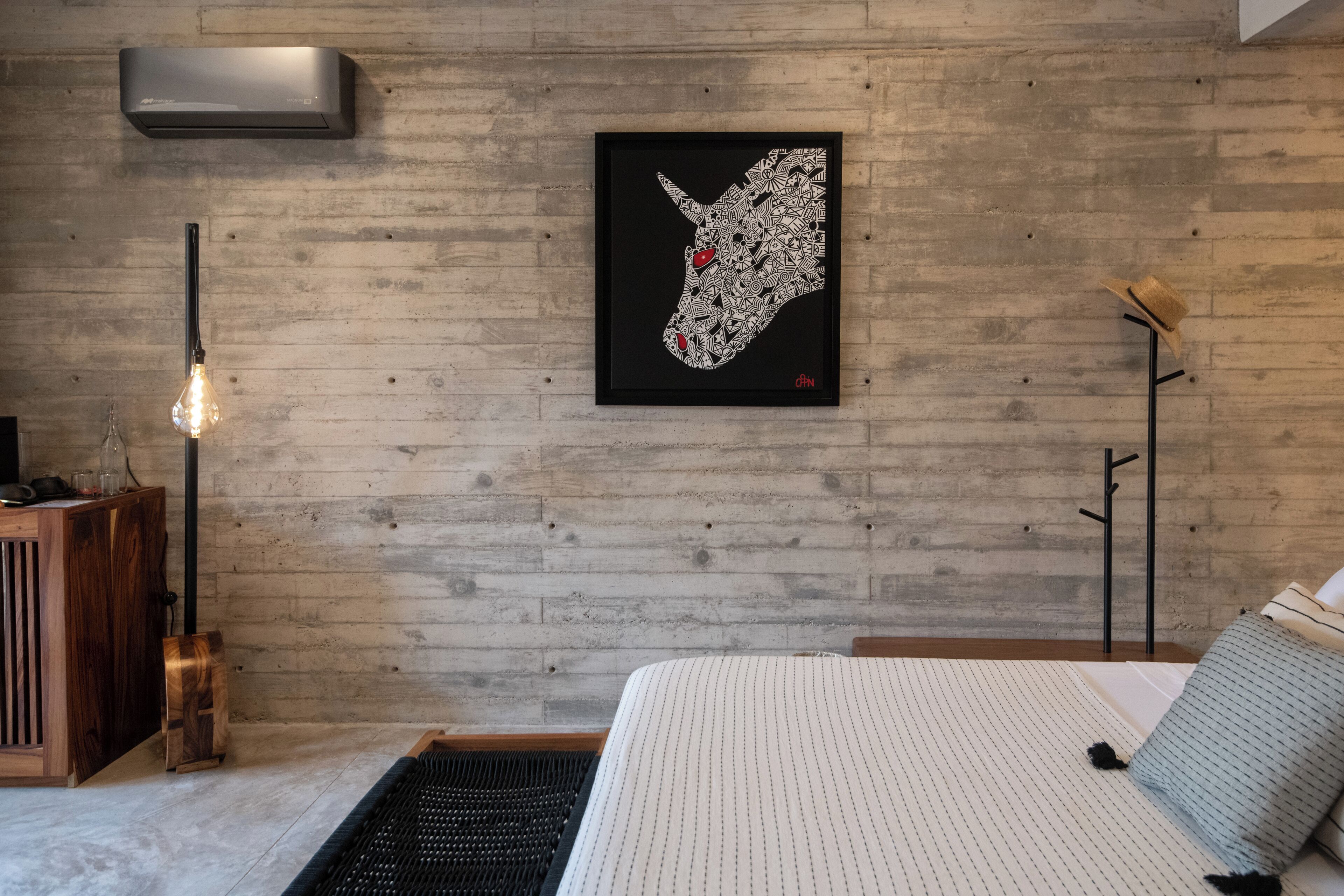 A modern bedroom with a wooden wall, a framed artwork, a bedside table, and a bed with a striped bedspread.