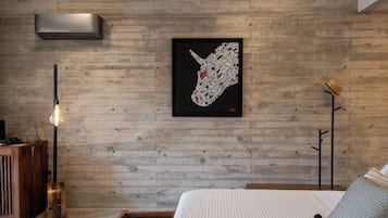 A modern bedroom with a wooden wall, a framed artwork, a bedside table, and a bed with a striped bedspread.