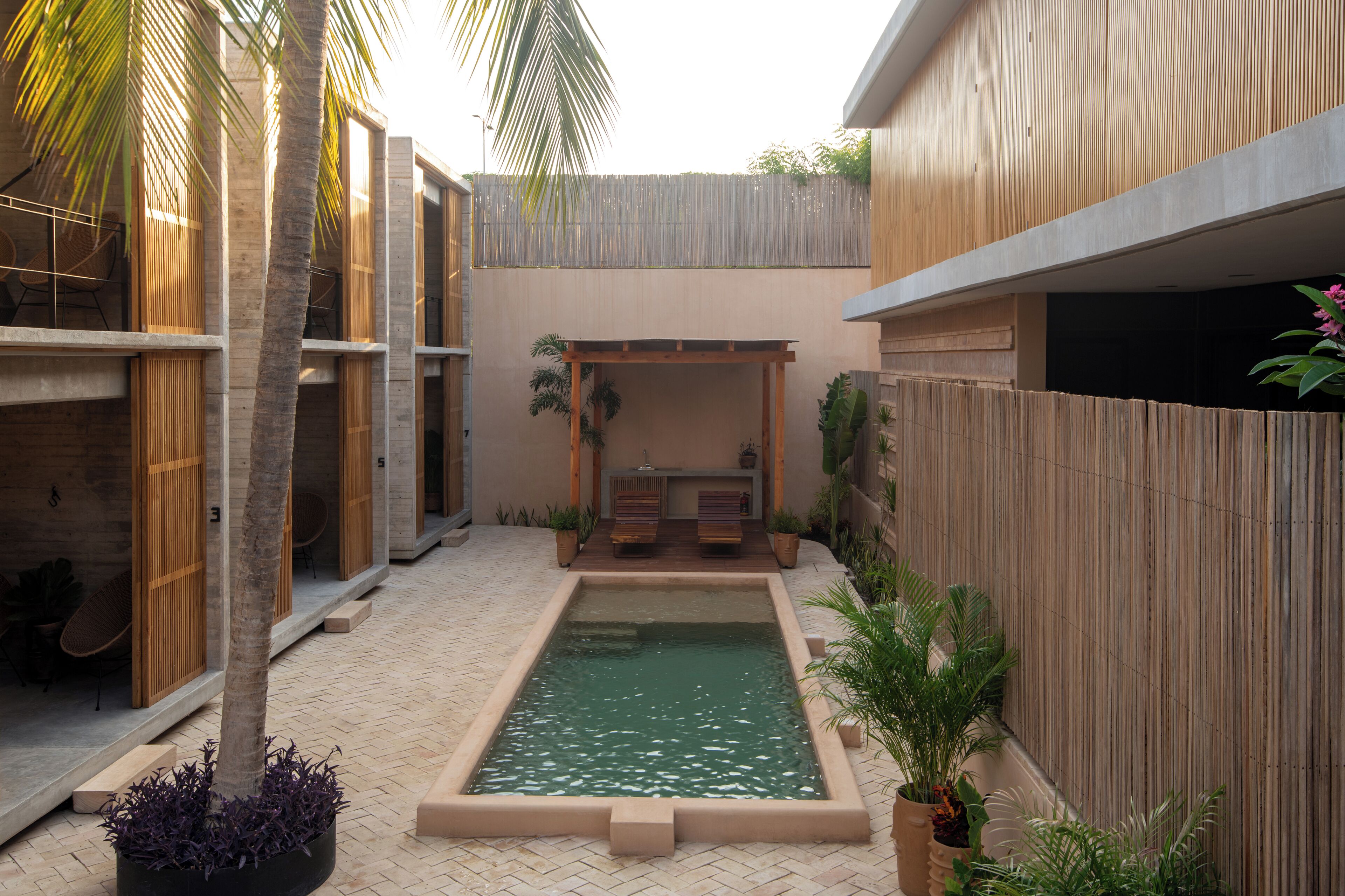 Ein moderner Poolbereich im Freien mit einer Holzpergola, Sitzgelegenheiten und Topfpflanzen.
