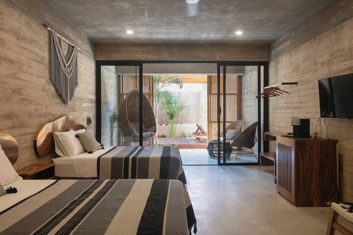 A modern hotel room with a large bed, a seating area with a chair and a table, a TV, and a view of the outside.