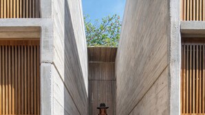 A person descending a staircase in a modern building with concrete walls and wooden slats. - Hotel JILOO Petite Maison (Santa Maria Colotepec)