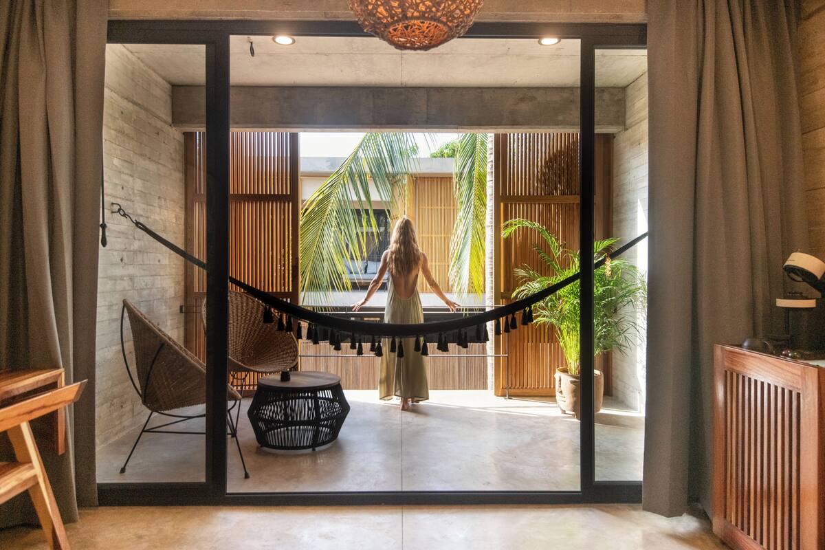 A room with a large sliding glass door leading to an outdoor area with a hammock, a wicker chair, and a round table.
